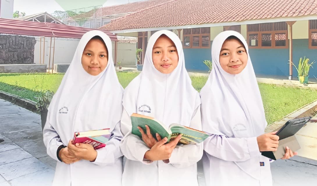Tiga santri putri membawa Al-Qur'an dan kitab di halaman Pondok Pesantren Al-Khairiyyah